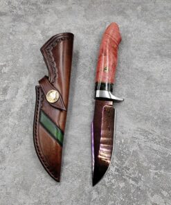 Damascus Steel bushcraft knife next to its leather sheath, lying on a grey concrete floor.