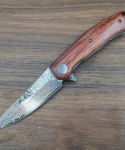 A folding damascus pocket knife lying on wood flooring.