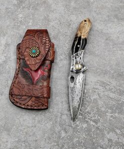 A folding damascus steel pocket knife next to its leather pouch, lying on a grey concrete floor.