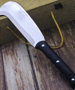 A hook machete leaning against a chest box and a wooden floor.