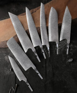 Seven kitchen knife blanks of varying design, displayed on a long wooden chopping board.